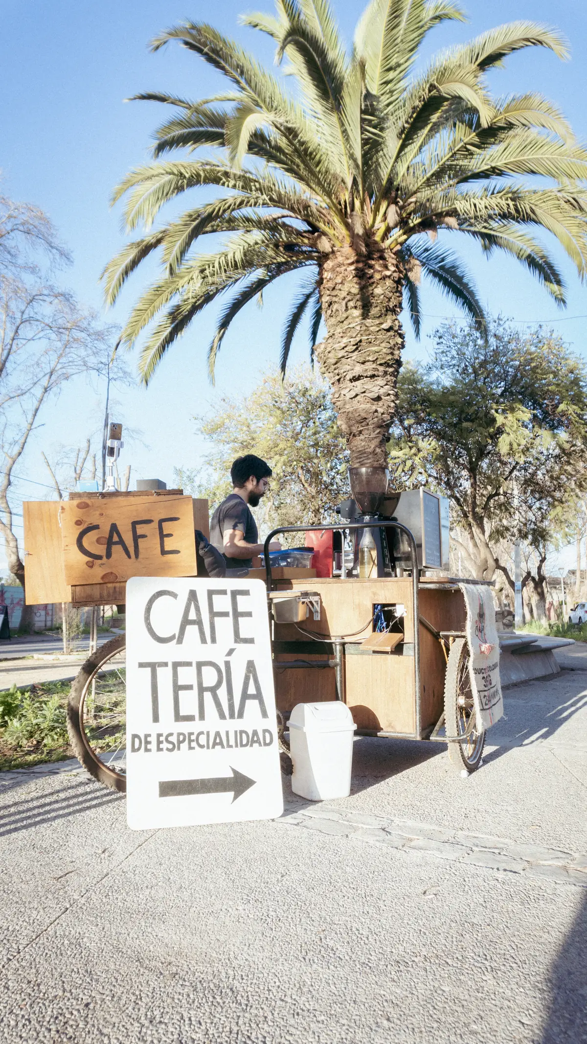 El triciclo de Amanecer Coffee estacionado bajo una palmera, con el letrero pintado a mano que dice Cafetería de especialidad.