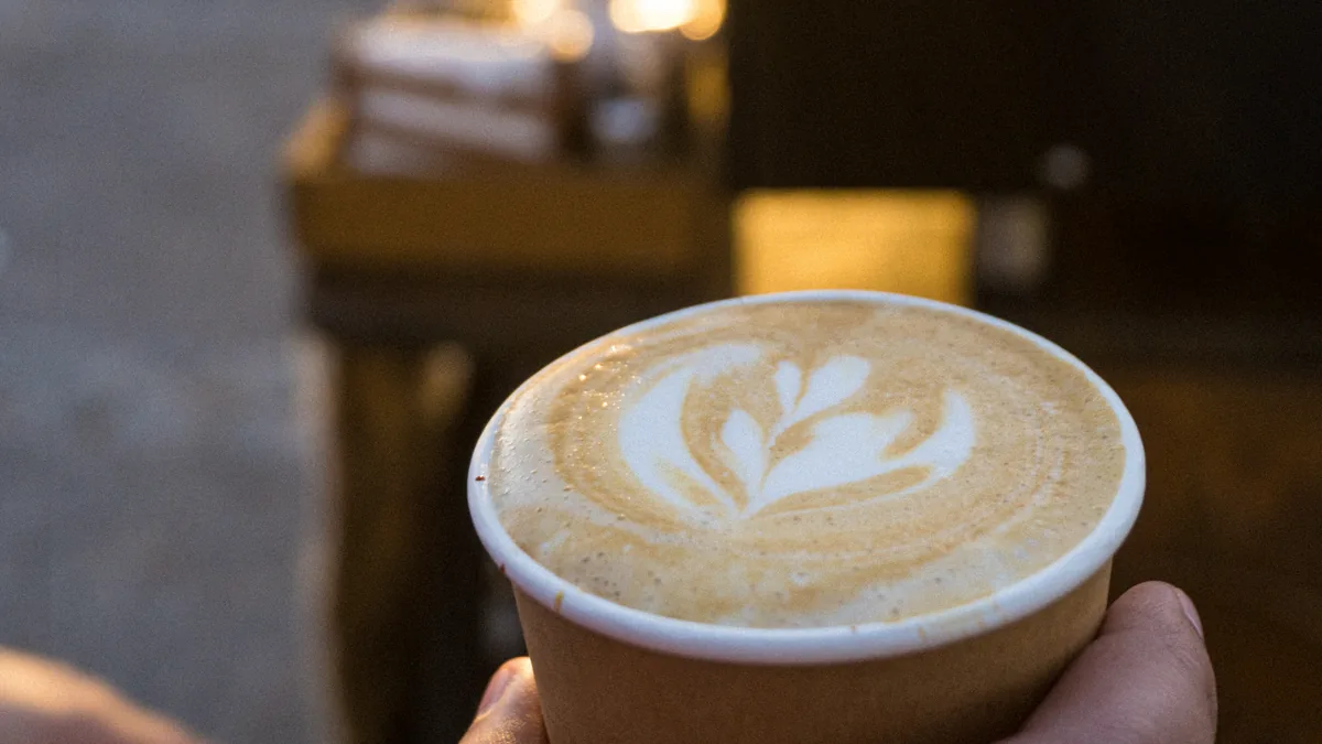 Latte con arte en la leche sostenido en la mano.